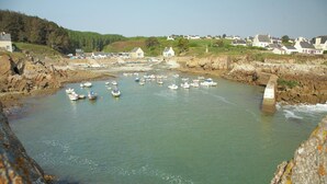 Un puerto costero con barcos amarrados, un puente y casas al fondo.