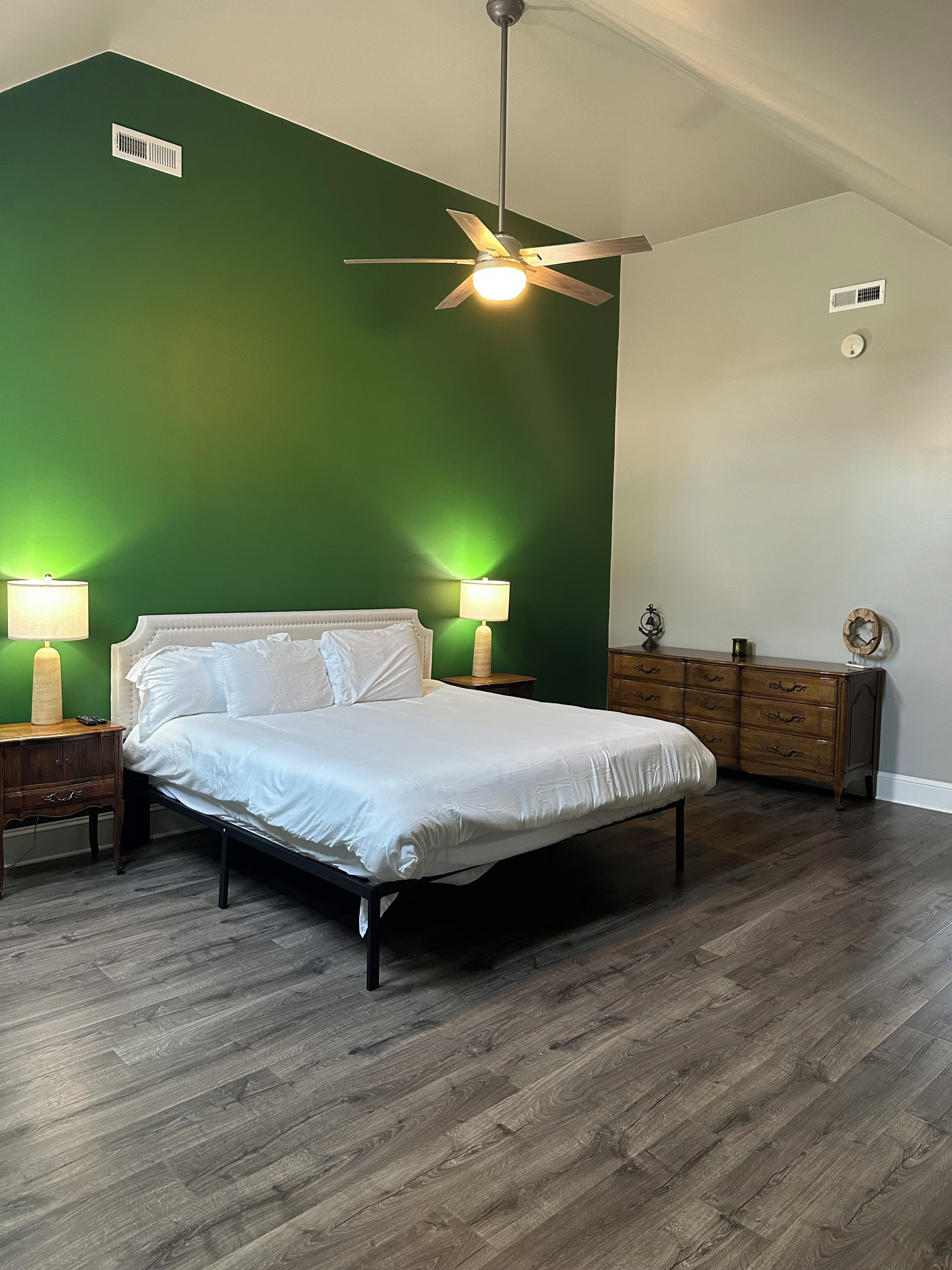 Une chambre à coucher comprenant un lit, deux lampes de chevet, un ventilateur de plafond, une commode et une table de chevet.