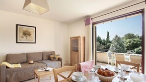 Ein möbliertes Wohnzimmer mit Sofa, einem Esstisch, der für das Frühstück gedeckt ist, und einem Balkon mit Blick auf Bäume.