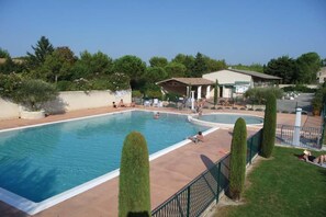 A swimming pool with a surrounding deck, a covered seating area, and a building in the background.
