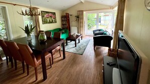 A spacious living area with a dining table, chairs, a sofa, and a television. - Chalet in Voorthuizen with indoor pool (Voorthuizen)