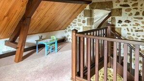 A rustic attic room with exposed wooden beams, a stone wall, and a wooden staircase. - Delightful holiday home with a large private swimming pool, perfect for families (Cérilly)