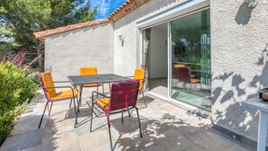 An outdoor patio with a table and chairs, a sliding glass door, and a textured wall. - Spacious villa with pool in Le Canet (Soleil d'Oc (Pouzols Minervois))