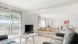 A modern living room with a sofa, a coffee table, and a TV. There is a dining area with a table and chairs. - Spacious villa with pool in Le Canet (Soleil d'Oc (Pouzols Minervois))