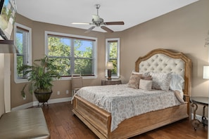 A bedroom with a large bed, a ceiling fan, a potted plant, and a window with blinds.
