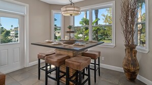 A kitchen with a central island, bar stools, a large vase, and large windows with a view of palm trees.