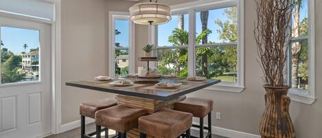 A kitchen with a central island, bar stools, a large vase, and large windows with a view of palm trees.