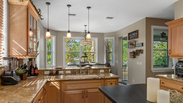 A kitchen with wooden cabinets, granite countertops, pendant lights, and a view of greenery outside.