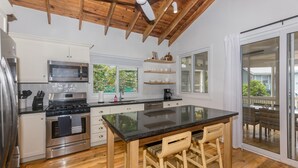 Una cocina moderna con suelo de madera, armarios blancos, una isla grande con taburetes y vistas a través de puertas de cristal.