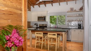 Una cocina moderna con vigas de madera, armarios blancos, una isla grande con taburetes de bar, un microondas y una cafetera.