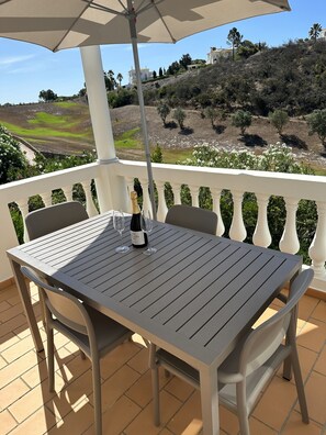 Une terrasse avec une table et des chaises, une bouteille de vin et un parasol.