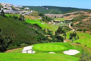 Un campo de golf con un club de campo, búnkeres de arena y una zona residencial al fondo.