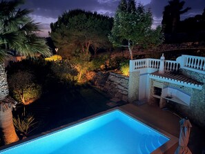 A swimming pool with a stone wall and a small patio area.