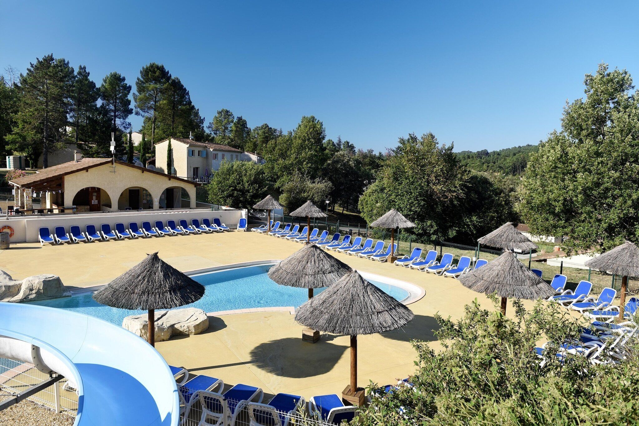A pool area with blue lounge chairs and thatched umbrellas.