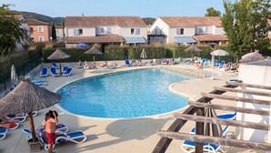Une piscine entourée de bâtiments aux toits recouverts de tuiles, avec des chaises longues et des parasols à proximité.