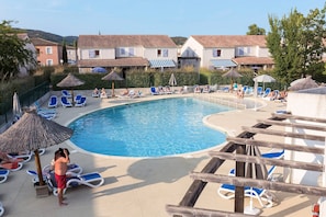 A swimming pool with lounge chairs and umbrellas, surrounded by buildings with tiled roofs. - Nature Retreat with Terrace (VALLON PONT D'ARC)