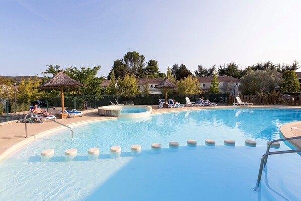 A swimming pool with lounge chairs and umbrellas, surrounded by a fence and trees.