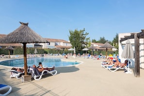 A poolside area with lounge chairs, umbrellas, and a thatched-roof structure.