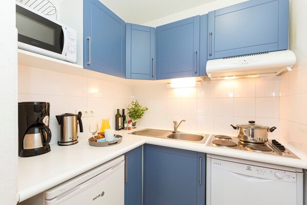 A modern kitchen with blue cabinets, white countertops, a microwave, a coffee maker, a kettle, a sink, and a stove.