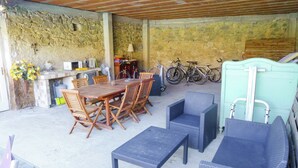En uteplats med en mur av sten, ett träbord med stolar, en blå soffa av rotting och cyklar som står lutade mot muren.