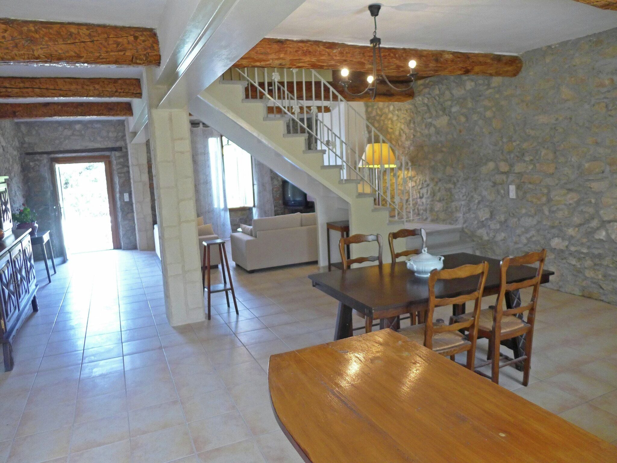 Amplia sala de estar con una mesa de comedor de madera, paredes de piedra, una escalera y una zona de estar acogedora.