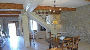 Un'ampia zona giorno con tavolo da pranzo in legno, pareti in pietra, una scala e un'accogliente angolo salotto.