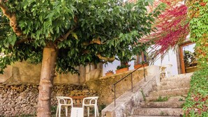 Una scala in pietra conduce a una sedia e un tavolo bianchi, posti di fronte a un muro, circondati da vegetazione e un altro muro in pietra.