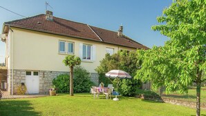 A house with a tiled roof, a stone foundation, and a well-maintained lawn. There is a table with chairs and an umbrella in the yard. - Cozy Garden Retreat Malemort (Malemort)