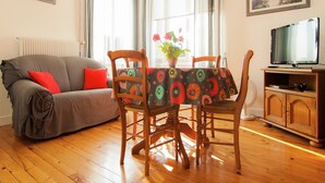 A living room with a sofa, two chairs, a table with a patterned tablecloth, a television on a wooden stand, and a painting on the wall. - Cozy Garden Retreat Malemort (Malemort)