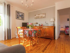 Una sala de estar acogedora con piso de madera, una mesa de comedor con sillas, un sofá, un televisor y un cuadro en la pared.