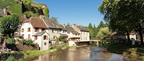 A riverside village with traditional stone buildings, a bridge, and lush greenery.