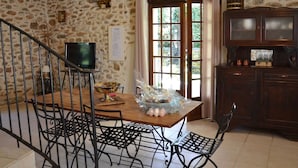 Un coin repas avec un mur en pierre, une table en bois, des chaises en métal, un téléviseur et un meuble.