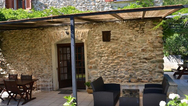 Un bâtiment en pierre doté d’un patio couvert, d’un espace extérieur aménagé avec des sièges et d’une table à manger.