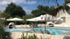 Un espace piscine agrémenté de chaises longues et de parasols, entouré de palmiers et de verdure.