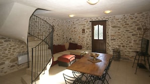 Un coin repas avec une table et des chaises en bois, un canapé, un mur en pierre, un escalier et une fenêtre donnant sur un paysage agréable.