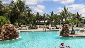 Une piscine à l’eau claire, entourée de chaises longues et de palmiers.