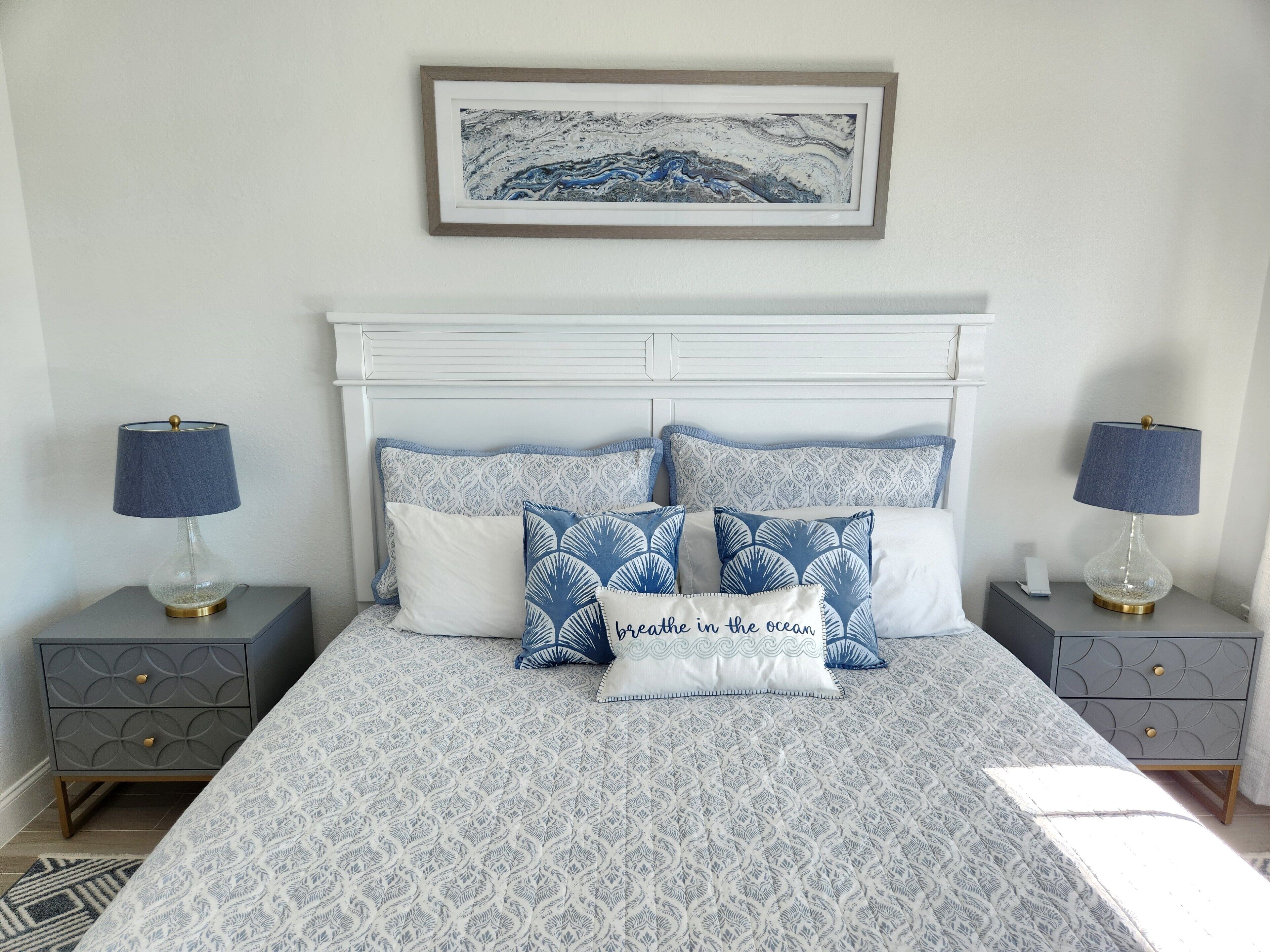 A neatly arranged bedroom with a patterned bedspread, matching pillows, and a framed artwork above the bed.