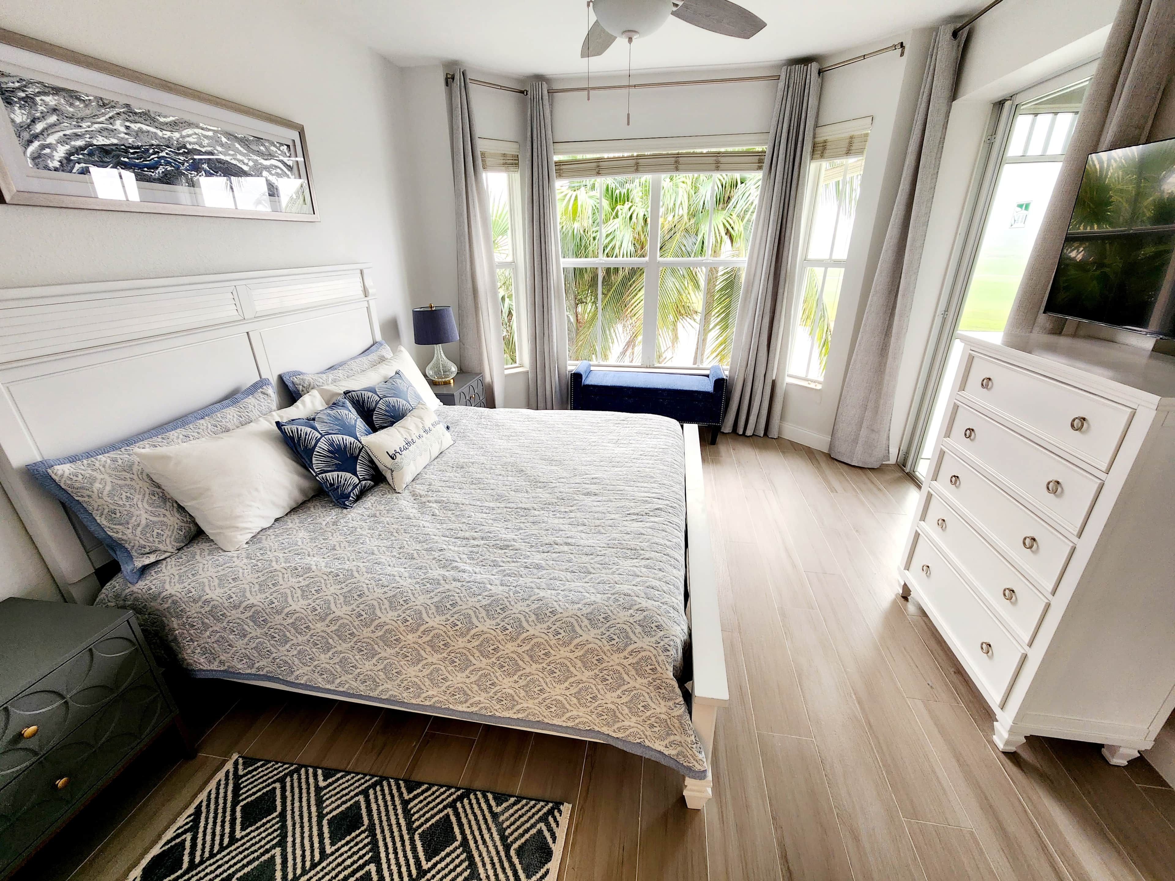 Un dormitorio con cama, mesita de noche, cómoda, televisor y ventana con cortinas.