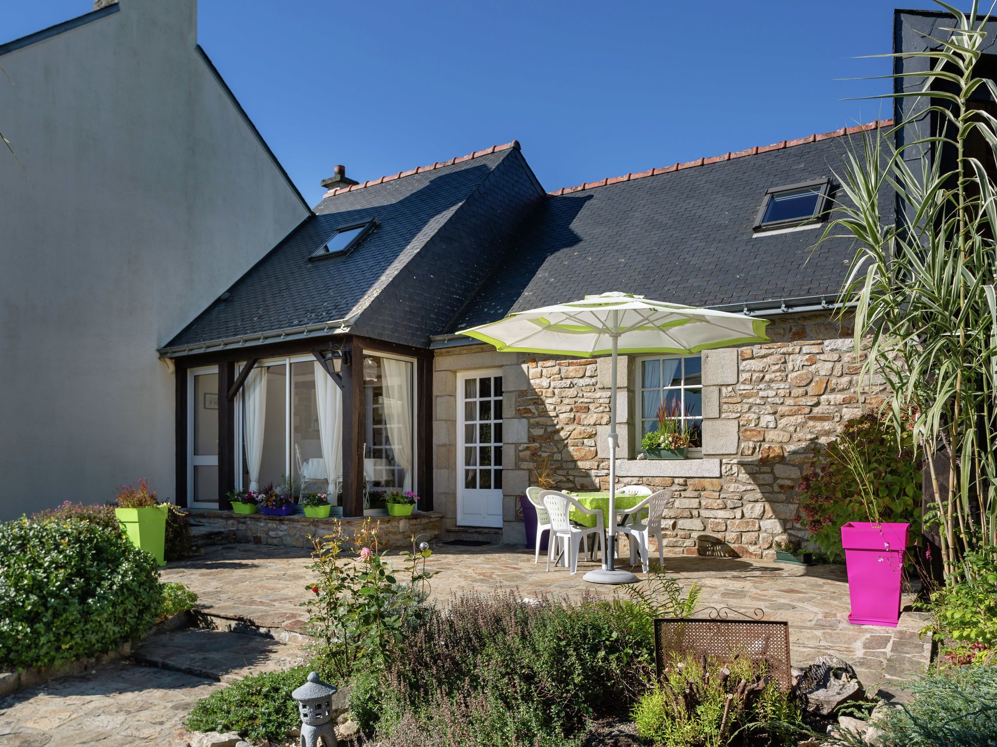 Una casa de piedra con techo de tejas, un porche cubierto con mobiliario exterior y un jardín con plantas en macetas.