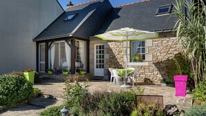 Ein Steinhäuschen mit Ziegeldach, einer überdachten Terrasse mit Gartenmöbeln und einem Gartenbereich mit Blumentöpfen.