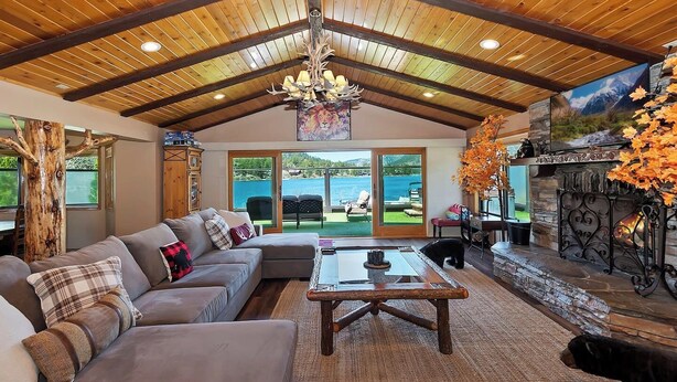 Amplia sala de estar con techo de madera, chimenea, ventanal grande con vistas panorámicas y un rincón de descanso acogedor.