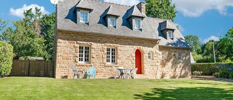 A stone house with a red door, multiple windows, and a well-maintained lawn.