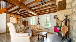 Ein geräumiges Wohnzimmer mit hoher Decke, freiliegenden Holzbalken, einem Steinkamin und einer Steinwand.