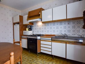 A compact kitchen with wooden cabinets, a stove, a sink, and a coffee maker. - Atmospheric Breton house with garden (Ploudalmezeau)