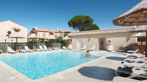 Piscina com espreguiçadeiras e um edifício com telhado de palha.