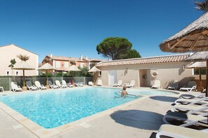 A swimming pool with lounge chairs and a thatched-roof building. - Maisonette in Aigues-Mortes near Flamingos (AIGUES MORTES)