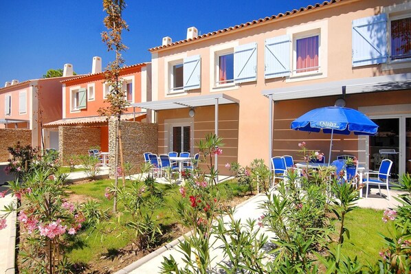 Un hôtel doté d’une terrasse, d’un mur en pierre et d’un parasol bleu.