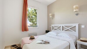 Um quarto com uma cama, uma janela com cortinas, uma mesa de cabeceira e uma luminária na parede.