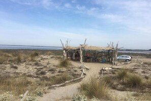 A beach with a simple wooden structure, a car, and sparse vegetation. - Maisonette in Aigues-Mortes near Flamingos (AIGUES MORTES)