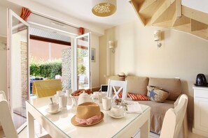 A bright room with a dining table set for breakfast, a sofa with cushions, and a view of greenery outside. - Maisonette in Aigues-Mortes near Flamingos (AIGUES MORTES)